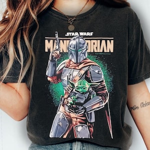 Pu&ograve; includere: T-shirt nera con una grafica di The Mandalorian che tiene Grogu di Star Wars. Il Mandaloriano &egrave; in armatura argentata, con un blaster. Grogu &egrave; verde e tenuto tra le braccia del Mandaloriano. Le parole "STAR WARS" e "MANDALORIAN" sono stampate sulla maglietta.
