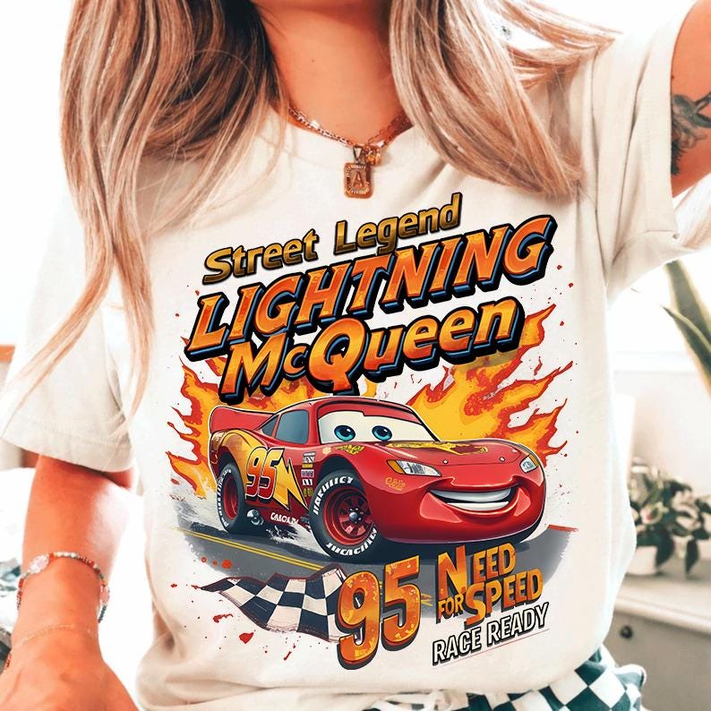 May include: White t-shirt featuring a graphic of Lightning McQueen from the Cars movie. The design includes the text "Street Legend Lightning McQueen" and "95 Need for Speed Race Ready". The red race car is set against a backdrop of flames.
