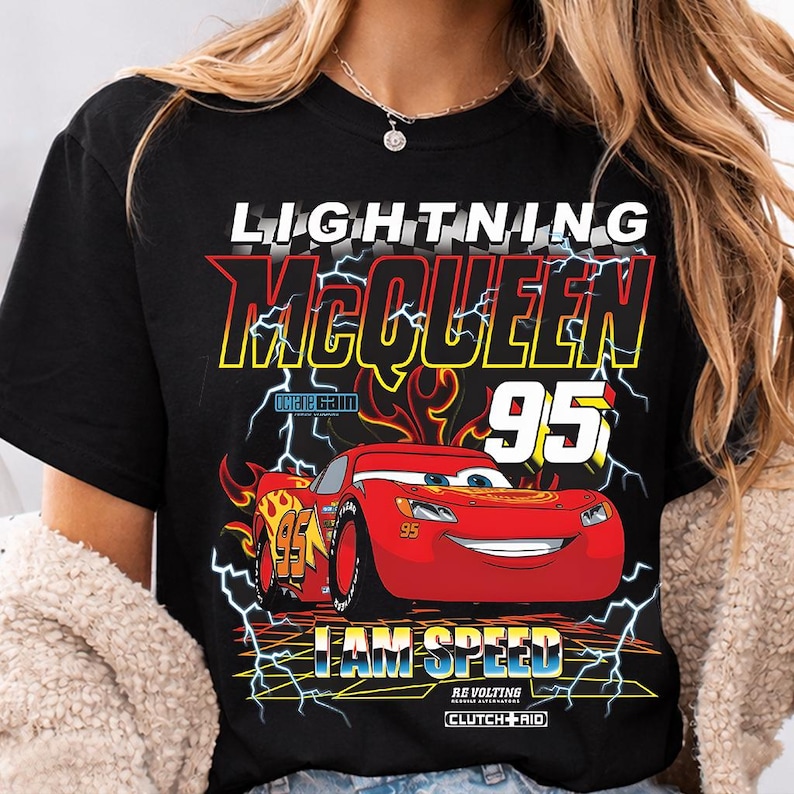 Op de afbeelding: Zwart T-shirt met een afbeelding van Lightning McQueen uit de film Cars. Het ontwerp bevat de tekst "LIGHTNING McQUEEN 95" en de woorden "I AM SPEED", samen met een rode raceauto-afbeelding.