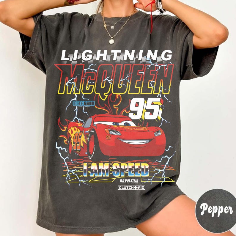 Op de afbeelding: Donkergrijs t-shirt met Lightning McQueen uit de film Cars. De afbeelding bevat de tekst "LIGHTNING McQUEEN 95" en "I AM SPEED" met een rode raceauto-illustratie. Het ontwerp bevat gele, rode en witte accenten.