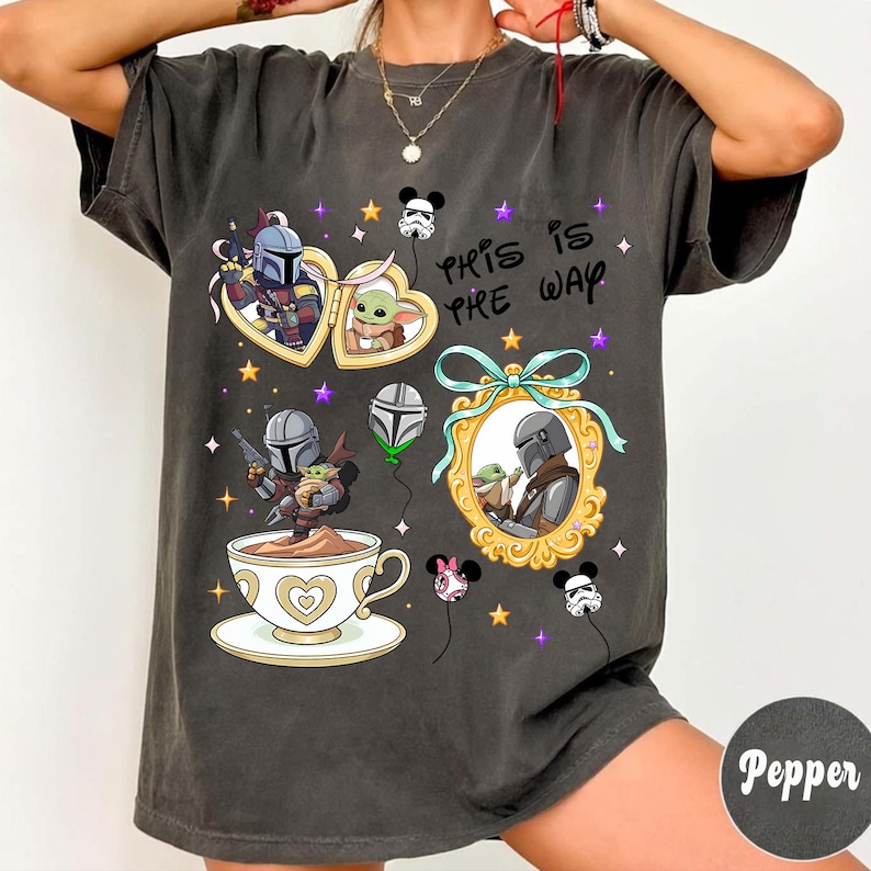 May include: Dark gray t-shirt featuring cartoon illustrations of characters from a popular space western. The design includes images within heart-shaped frames, a teacup, and balloons. The text "THIS IS THE WAY" is also present.