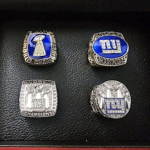 May include: Four championship rings with intricate designs. Two rings feature a blue background with the letters "NY" and the word "Champions". The other two rings have a silver finish with the words "World Champions".