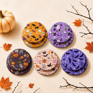 May include: Five sets of circular coasters featuring various Halloween-themed patterns including pumpkins, ghosts, bats, skulls, and witch hats in orange, purple, and pastel color palettes. Each set consists of two stacked round coasters.