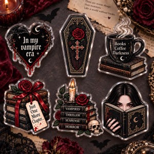 May include: A set of six acrylic pins featuring gothic themes including a heart with the text In my vampire era, a coffin with a red rose and cross, a coffee mug on books, a stack of books with a red bow, a candle on books, and a person reading.