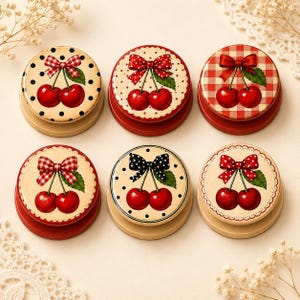 May include: Six circular phone grips featuring cherry illustrations. Each grip displays a pair of red cherries with green leaves and a decorative bow. The backgrounds vary, including cream with black polka dots, red with white dots, and red gingham.