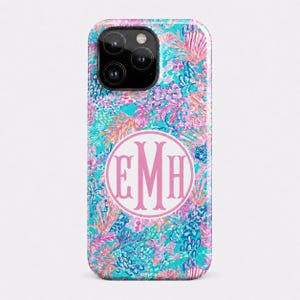 May include: A smartphone case featuring a vibrant, multi-colored pattern of coral, seashells, and aquatic flora in shades of turquoise, pink, and purple. Centered on the case is a white circular emblem containing the pink monogram letters EMH.