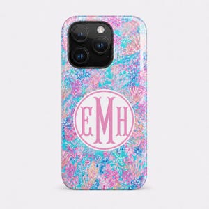 May include: A smartphone case featuring a vibrant, multi-colored floral and abstract pattern in shades of bright pink, turquoise, and blue. Centered on the back is a white circular emblem containing the large, stylized pink monogram letters EMH.