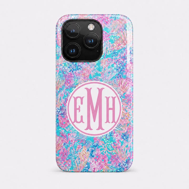 May include: A smartphone case featuring a vibrant, multi-colored floral and abstract pattern in shades of bright pink, turquoise, and blue. Centered on the back is a white circular emblem containing the large, stylized pink monogram letters EMH.