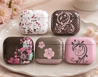 May include: Five rectangular earbud cases featuring various designs: a white case with pink floral swirls, a brown case with white polka dots and swirls, a dark brown case with pink hibiscus flowers, a grey case with pink cherry blossoms, and a pink case with black swirls and dots.