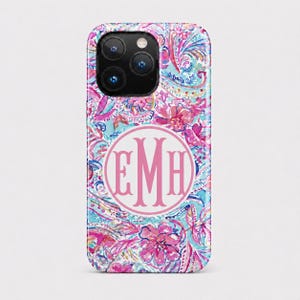 May include: A smartphone case featuring a vibrant, multi-colored floral and paisley pattern in shades of pink, blue, and white. Centered on the back is a circular white emblem containing the large, stylized pink monogram letters EMH.
