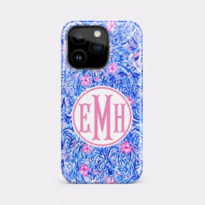 May include: A smartphone case featuring a vibrant blue and white botanical pattern with small pink floral accents. Centered on the back is a circular white emblem with a pink border containing the large, stylized pink monogram letters EMH.