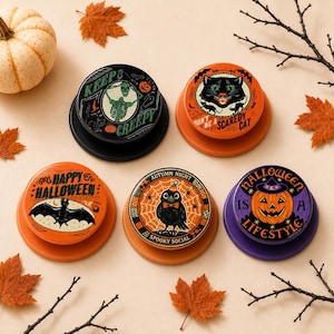 May include: Five circular phone grips featuring Halloween designs. One shows a skeleton with the text KEEP IT CREEPY, one a black cat with DON'T BE A SCAREDY CAT, one a bat with HAPPY HALLOWEEN, one a crow with AUTUMN NIGHT SPOOKY SOCIAL, and one a pumpkin with HALLOWEEN IS A LIFESTYLE.