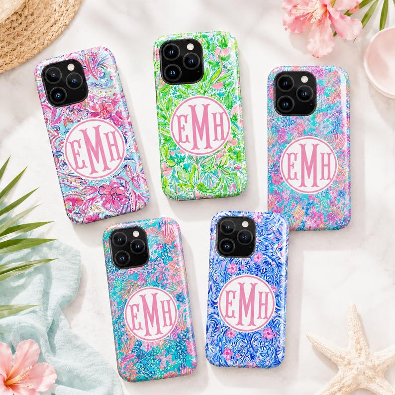 May include: Five smartphone cases featuring vibrant, multi-colored floral and abstract patterns. Each case displays a circular white emblem in the center containing the pink monogram letters EMH. The cases have black camera lens cutouts.