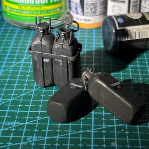May include: Miniature black water bottles, some with open lids, and a carrier. The bottles are labelled with "Trasser" and "5L". The bottles are on a green cutting mat with measurements.