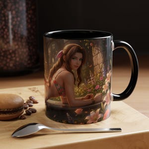Könnte beinhalten: Schwarz-weiße Keramik-Tasse mit einer Frau in einem geblümten Bikini, umgeben von Blumen und einer Steinmauer. Die Tasse hat einen schwarzen Innenraum und einen Griff. Ein Löffel und ein Macaron befinden sich im Vordergrund.