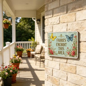 May include: A rectangular metal sign with the text "Fairies Enchant This Area" and illustrations of a yellow and blue butterfly, and red roses. The sign is mounted on a brick wall, with a porch and potted flowers in the background.