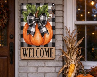 May include: A rectangular metal sign featuring a large orange pumpkin with green leaves and a black and white buffalo check bow. The background is a black and white buffalo check pattern. The word WELCOME is printed in black on a tan base.