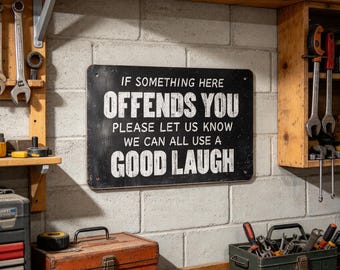 May include: A rectangular black metal sign with white text that reads: IF SOMETHING HERE OFFENDS YOU PLEASE LET US KNOW WE CAN ALL USE A GOOD LAUGH. The sign features a distressed finish and four mounting holes, one in each corner.