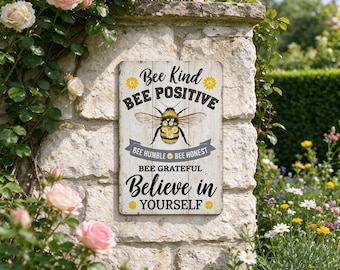May include: A rectangular metal sign with a wood-grain background featuring a central bumblebee illustration surrounded by the text Bee Kind, Bee Positive, Bee Humble, Bee Honest, Bee Grateful, and Believe in Yourself with small yellow flowers.