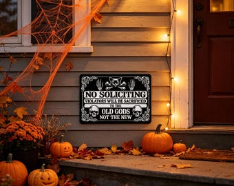 May include: A rectangular black sign with white text and graphics. The sign features a cat head, skeletal hands, and two skulls. The text reads: NO SOLICITING VIOLATORS WILL BE SACRIFICED TO THE OLD GODS NOT THE NEW. The sign has a decorative border.