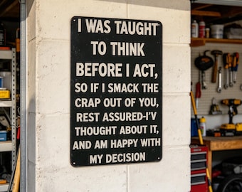 May include: A rectangular black metal sign with white text that reads: I WAS TAUGHT TO THINK BEFORE I ACT, SO IF I SMACK THE CRAP OUT OF YOU, REST ASSURED-I'V THOUGHT ABOUT IT, AND AM HAPPY WITH MY DECISION. The sign has rounded corners.