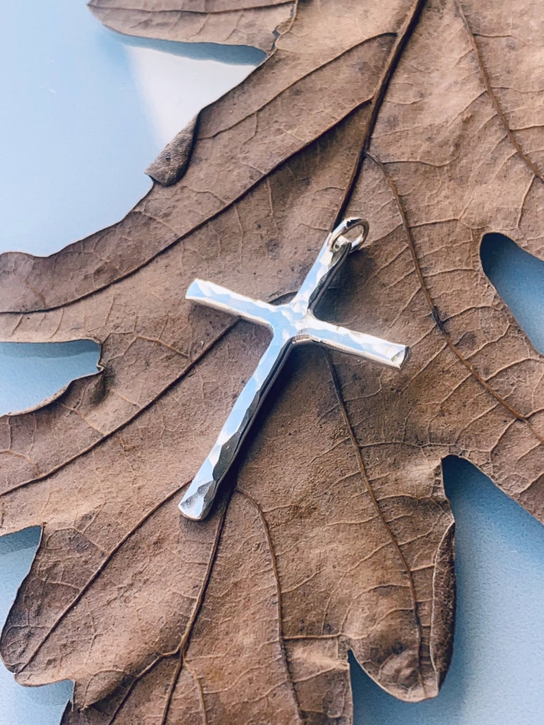 May include: A silver hammered cross pendant on a dried brown leaf.