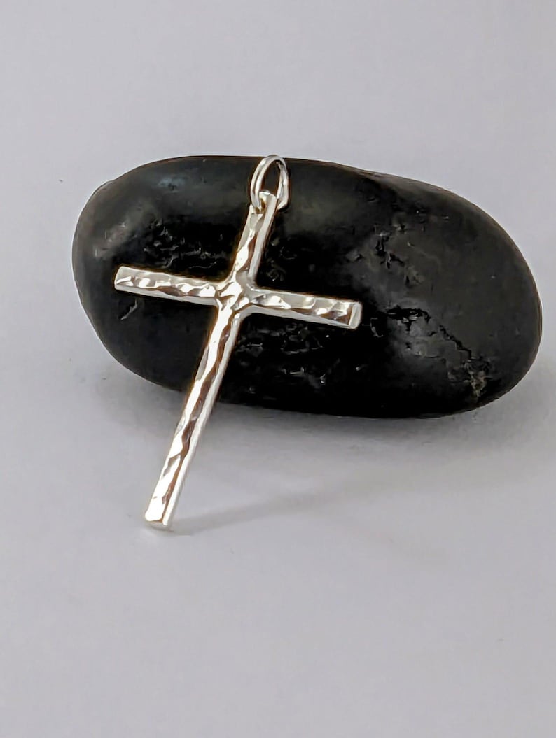May include: A silver hammered cross pendant charm. The cross is textured and has a simple design.