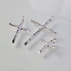 May include: Three silver cross pendants of different sizes. The crosses are hammered and have a textured surface.