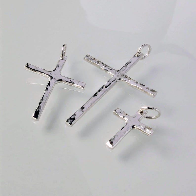 May include: Three silver cross pendants of different sizes. The crosses are hammered and have a textured surface.