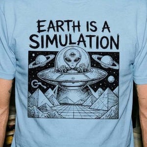 Puede incluir: Camiseta azul claro con el texto "EARTH IS A SIMULATION" sobre un gráfico en blanco y negro de un OVNI con un extraterrestre. El diseño incluye pirámides y planetas.