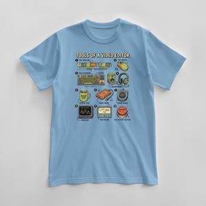 May include: Light blue t-shirt featuring a graphic titled "TOOLS OF A VIDEO EDITOR." The graphic includes illustrations of video editing tools such as a timeline, mouse, keyboard, headphones, and the "EXPORT" button.