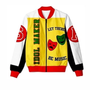 May include: A bomber jacket featuring a yellow front panel with the text IDOL MAKER and LET THERE BE MUSIC, accompanied by red and green theatre masks. The sleeves are white with black accents and red cuffs, featuring red circular patches with white letters.