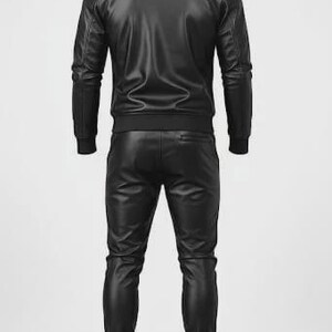 May include: A black leather tracksuit, consisting of a zip-up jacket and matching pants. The jacket has a stand-up collar and ribbed cuffs and hem. The pants have a jogger style with ribbed cuffs. The outfit is made of a shiny, faux leather material.