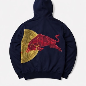 Puede incluir: Sudadera con capucha azul marino con un gr&aacute;fico de toro rojo y un dise&ntilde;o de espiral dorado en la espalda. El toro est&aacute; representado en posici&oacute;n de carga. La sudadera tiene una capucha con cord&oacute;n y pu&ntilde;os y dobladillo acanalados.