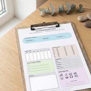 Può includere: Un pianificatore settimanale "Low-Energy Weekly Planner" su una clip board di legno. Include sezioni per attività, monitoraggio dell'umore e un'area per il brainstorming. Lo schema dei colori comprende blu, verde e rosa.
