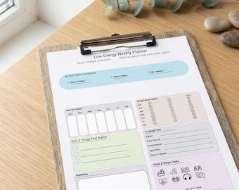 May include: A weekly planner on a wooden clipboard. The planner has sections for battery charging, weekly tasks, and a brain dump. The text "Low-Energy Weekly Planner" is at the top. The planner is on a wooden table with greenery.
