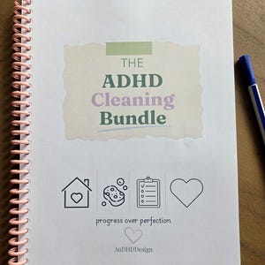 Op de afbeelding: Een spiraalgebonden notitieboek met een lichtroze spiraal en de tekst THE ADHD Cleaning Bundle in groen en paars. Daaronder staan iconen van een huis, spons, checklist en hart, met de tekst progress over perfection en AuDHDDesign.