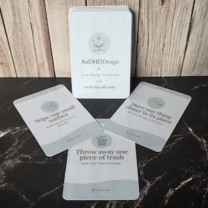 May include: A deck of white rectangular task cards titled AuDHDDesign Low Energy Task Cards. The cards feature gray icons and text instructions such as Wipe one small surface, Move one thing closer to its place, and Throw away one piece of trash.