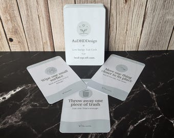 May include: A deck of white rectangular task cards titled AuDHDDesign Low Energy Task Cards. The cards feature grey icons and text instructions such as Wipe one small surface, Move one thing closer to its place, and Throw away one piece of trash.