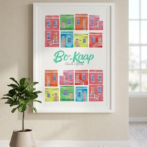 Può includere: Una stampa ad acquerello incorniciata con case colorate a Bo-Kaap, Sudafrica. Le case sono dipinte in vivaci tonalità di rosso, verde, blu e giallo. Il testo "Bo-Kaap South Africa" è scritto in un carattere verde acqua.