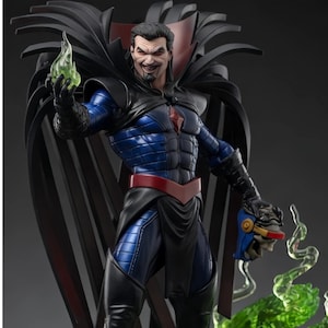 May include: A detailed collectible figurine of a male character with dark hair and a goatee, wearing a blue and black armored suit with a red belt and a large black cape. The figure holds a glowing green flame in one hand and a blue helmet in the other.