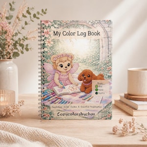 Könnte beinhalten: Ein spiralgebundenes Notizbuch "My Color Log Book" mit einer Illustration eines Bären-Feen und eines Welpen. Der Einband enthält den Text "Swatches, Color Codes & Creative Inspiration" und "Cozycolorsbychar". Das Buch liegt auf einer Holzoberfläche.