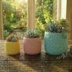 May include: Three colorful ceramic planters with succulents. The planters are yellow, pink, and teal, each with a detailed geometric pattern. The plants have various green hues, and the scene is set on a wooden table with a blurred outdoor background.
