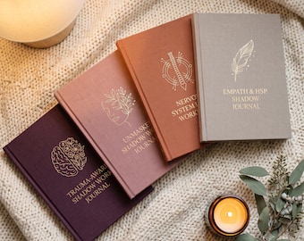 Puede incluir: Cuatro diarios de tapa dura en morado, rosa empolvado, terracota y gris claro, cada uno con texto y arte lineal en lámina dorada. Los títulos son Trauma-Aware Shadow Work Journal, Unmasked Shadow Work Journal, Nervous System Workbook y Empath & HSP Shadow Journal.