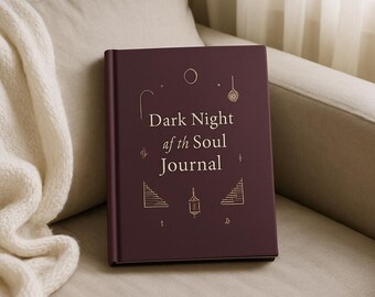 May include: A dark maroon hardcover journal with gold foil line art illustrations and the text Dark Night of the Soul Journal printed on the front cover. The design includes small celestial and geometric symbols surrounding the central title text.