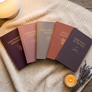 May include: Five hardcover books with gold foil lettering and symbols on their covers. The titles are Dark Feminine Awakening, Inner Child Healing, Perfectionism Shadow, Money Shadow, and Dark Night of the Soul, arranged in a fan shape on fabric.