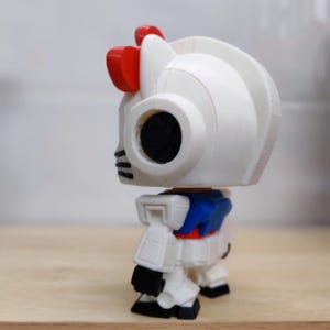 May include: A white robot figurine with red accents, including a bow on its head. The figurine has a black eye and a blue and red torso. A collectible item, likely a toy or decorative piece.