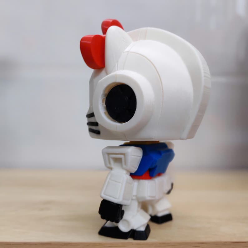 May include: A white robot figurine with red accents, including a bow on its head. The figurine has a black eye and a blue and red torso. A collectible item, likely a toy or decorative piece.