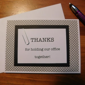 May include: A gray and white polka dot card with a black border and a black and white paperclip. The card says "THANKS for holding our office together!"