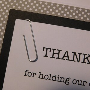 May include: A white card with black text that reads "THANKS for holding our offic", a silver paper clip is attached to the top of the card.